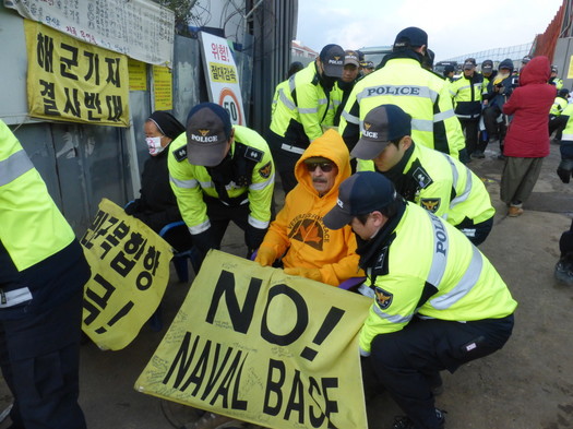 Veterans For Peace delegation organizer Tarak Kauff is set down at the side of the base entrance by South Korean police. Photo by ELLEN DAVIDSON